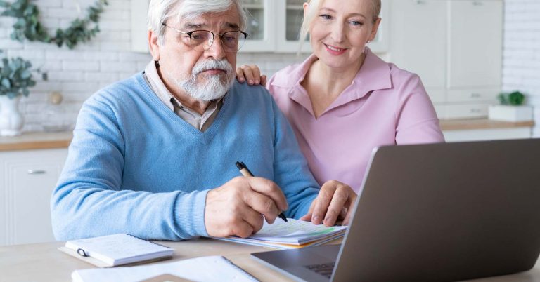 Senior couple reviewing documents beside a laptop at home