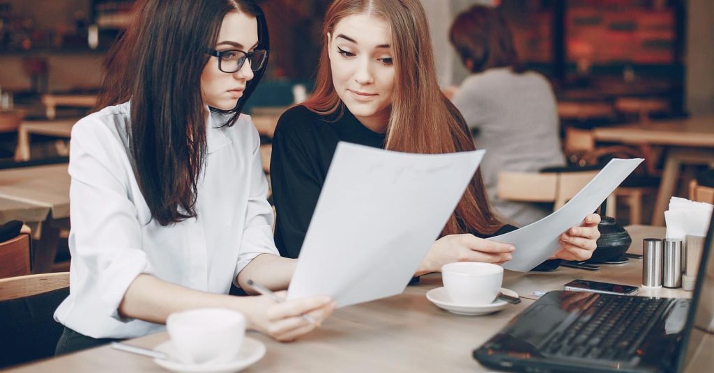 Two women comparing printed documents at a table
