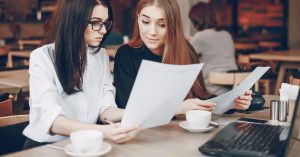 Two women comparing printed documents at a table