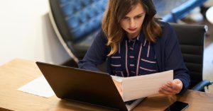 Woman reviewing life insurance policy documents beside a laptop